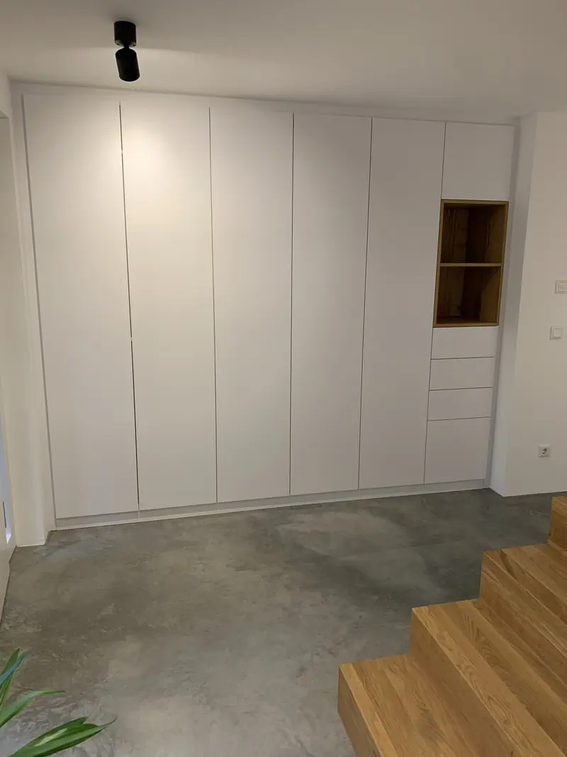 Raumhoher weißer Einbauschrank mit offenem Fach und Schubladen neben einer Holztreppe