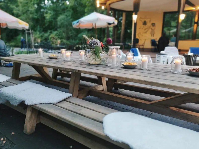 Lange Tischgarnitur aus Holz mit Bänken und Sitzkissen unter einem Pavillon im Grünen