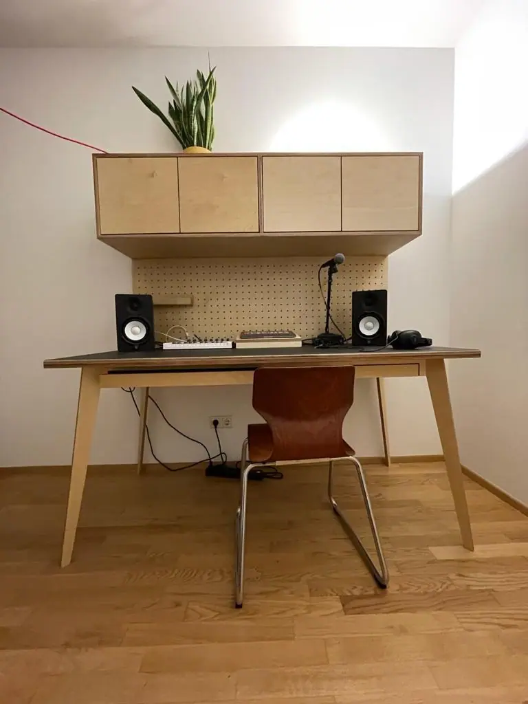 Schreibtisch mit Hängeschränken aus hellem Holz und Lochwand über dem Arbeitsplatz